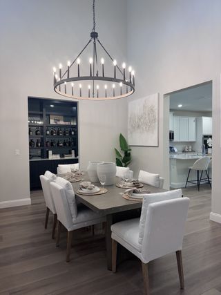 Elegant dining room with a grand chandelier, cushioned chairs, and warm wooden flooring. Modern and inviting space.