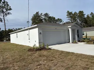 A modern white home with a spacious driveway and minimal landscaping in The Collection at Ocklawaha by Century Complete (Ocklawaha, FL).