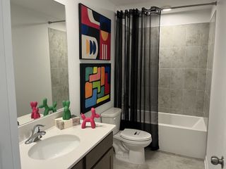 A modern bathroom with abstract art, gray-tiled tub, sleek vanity, and playful decor accents.