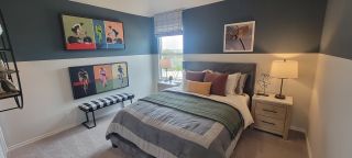 A cozy bedroom featuring a stylish gray bed, modern artwork, and a plaid bench under a large window.