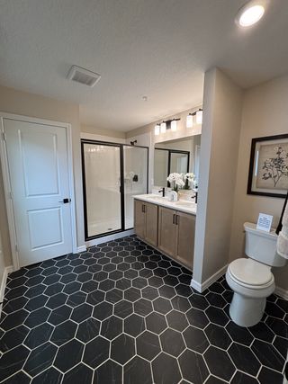 A modern bathroom featuring hexagonal tile flooring, a glass-enclosed shower, dual vanity, and sleek lighting.