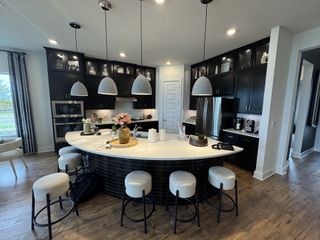 Model Home A modern kitchen featuring sleek black cabinets, a curved island with barstools, and stylish pendant lighting.