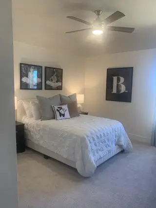A cozy bedroom with soft lighting, elegant wall art, a plush bedspread, and a modern ceiling fan.
