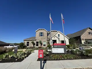 A beautiful brick home with a landscaped front yard, flags, and modern entrance in 6 Creeks by Taylor Morrison (Kyle, TX).