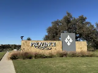 Street view The Provence community entrance sign, featuring stone accents and decorative landscaping, marking the welcoming entry to Provence by Drees Custom Homes in Austin, TX.