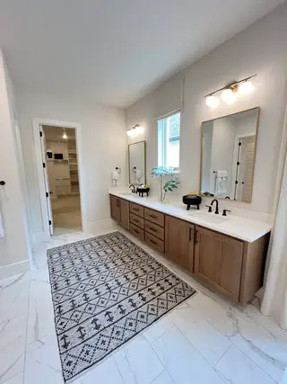 A spacious bathroom featuring a wood vanity, dual mirrors, and chic lighting with a patterned rug for added style.
