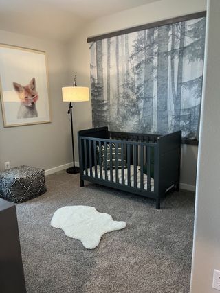 A cozy nursery with a dark crib, forest mural, and fox artwork, featuring plush carpet and elegant lighting.