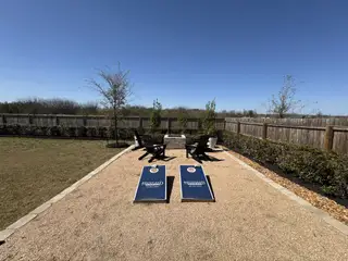 A serene backyard with a cornhole game, seating area, and lush landscaping in Venado Crossing by Highland Homes (Cibolo, TX).