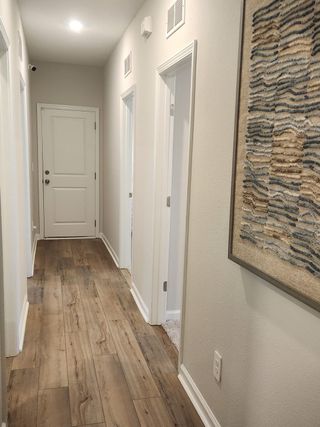 A modern hallway with wood flooring, soft lighting, and contemporary textured artwork on the wall.