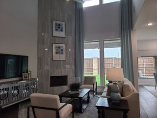 Model Home A modern living room with a tall tiled fireplace, elegant furniture, and large windows with soft drapes.