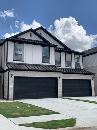 A sleek duplex-style townhome with contemporary black and white finishes and lush green landscaping in Whitestone Preserve by Pulte Homes (Cedar Park, TX).