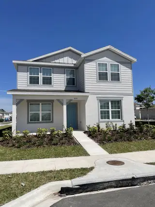 A charming two-story home with a welcoming blue door, modern siding, and manicured landscaping in Winding Meadows by Pulte Homes (Apopka, FL).