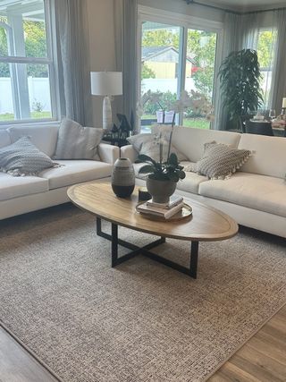 A cozy living room featuring white sofas, a wooden coffee table, and large windows overlooking a lush garden.