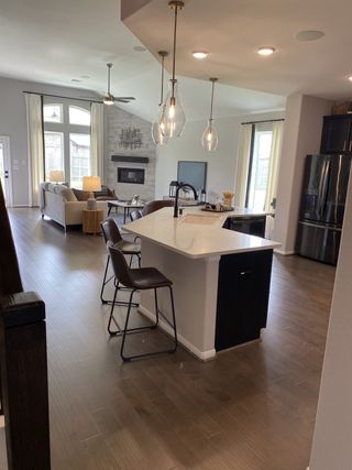 A modern open-concept kitchen and living area with sleek pendant lighting, a central island, and warm wooden floors.
