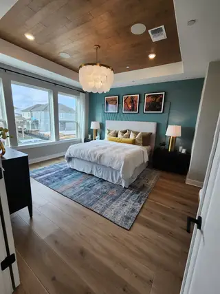 A stylish bedroom with a teal accent wall, modern lighting, and large windows providing natural light.