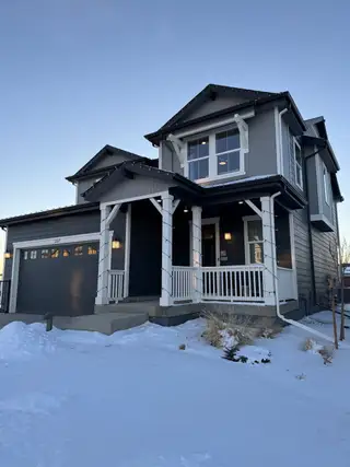 A charming gray home with a welcoming porch and snowy yard in Farmlore Villas by KB Home (Brighton, CO).