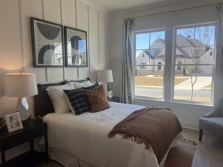 A cozy bedroom with modern artwork, large windows, and elegant decor, featuring a plush bed with stylish accent pillows.