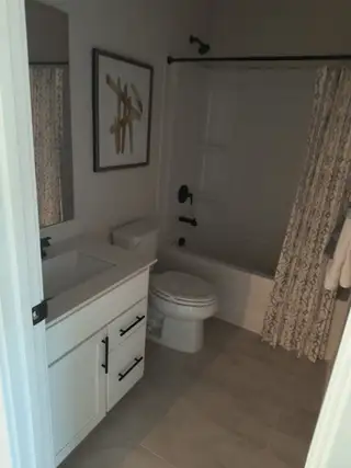 A modern bathroom with sleek white cabinetry, a shower-tub combo, and stylish artwork on the wall.