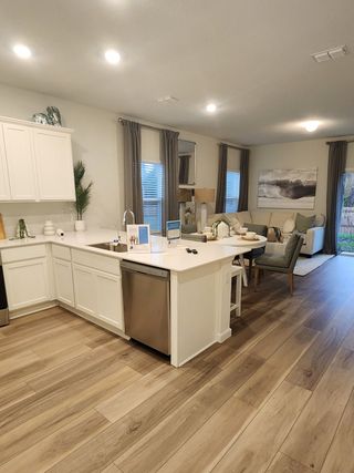 Model Home A modern open-concept kitchen and living area with sleek white cabinetry, wood flooring, and elegant decor.