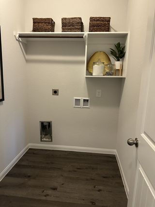 A tidy laundry room with dark wood floors, open shelving with baskets, and space for a washer and dryer.