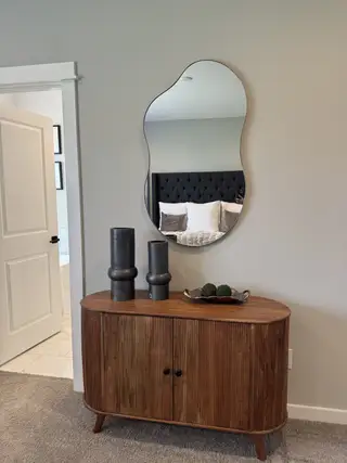 A modern interior with an artistic mirror above a wooden console, complemented by sleek decor.