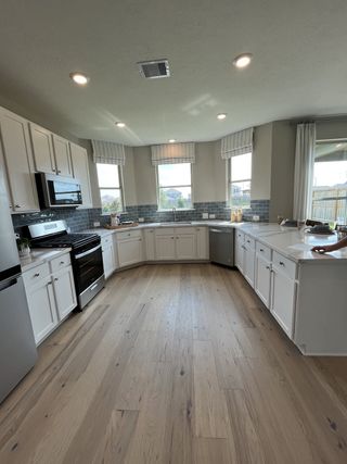 Model Home A spacious kitchen with light wood flooring, white cabinets, modern appliances, and ample natural light.