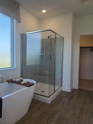 Model Home A contemporary bathroom featuring a freestanding tub, glass shower, and wood-look tile flooring with ample natural light.