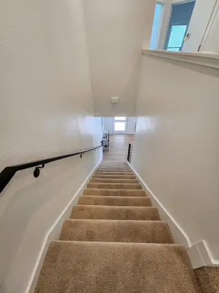 A cozy carpeted staircase with sleek black handrail leading to a bright, airy hallway and wooden flooring.