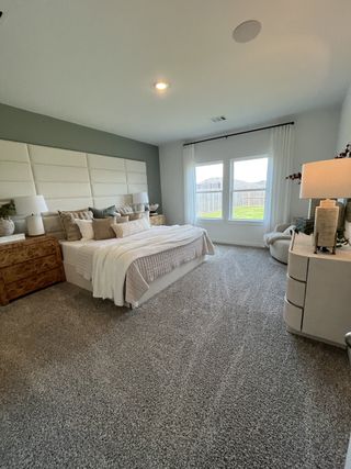 A cozy bedroom with a plush gray carpet, modern furnishings, and a large window letting in natural light.