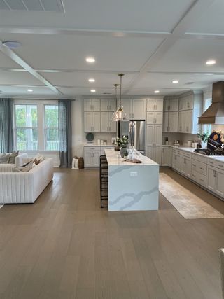 A sleek kitchen with a spacious island, modern lighting, and hardwood floors, leading into an open and airy living room.