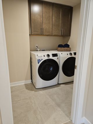A modern laundry room featuring sleek cabinets, a front-load washer and dryer, and elegant tile flooring.