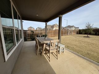 A covered patio in Salerno by KB Home (Round Rock, TX) features a wooden dining set, offering an inviting outdoor space overlooking a spacious backyard.