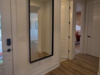 A welcoming hallway with wood floors, tall mirror, and white paneled doors leading to a cozy room with neutral decor.