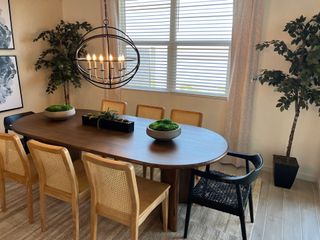 A cozy dining area with a wooden table, woven chairs, a modern chandelier, and lush greenery accents.