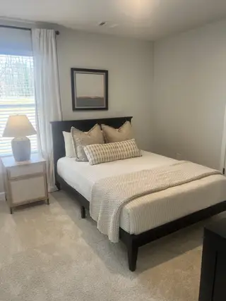 A cozy bedroom features a dark wood platform bed with neutral bedding, complemented by a matching nightstand and a framed abstract artwork.