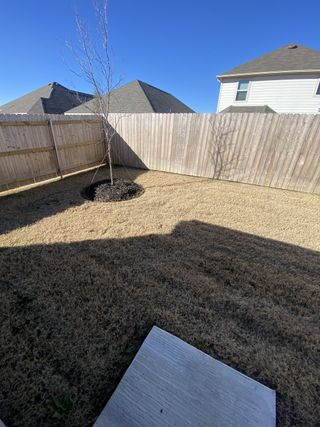 A compact backyard enclosed by a wooden fence, featuring a concrete patio and dry grass.