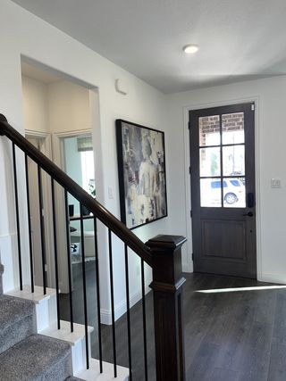 Model Home A bright entryway with dark wood floors, modern railing, and abstract art, leading to a cozy room.