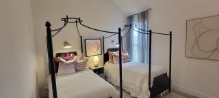 A cozy bedroom with twin beds, elegant iron frames, and stylish decor, featuring warm lighting and soft curtains.