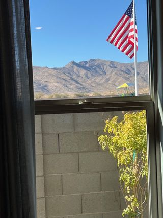 A breathtaking mountain view through a window, complete with a vibrant American flag and lush greenery in the foreground.