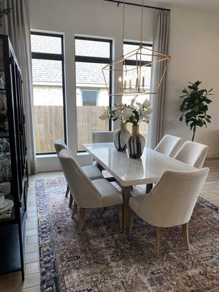 Model Home Elegant dining room with a marble table, modern chandelier, and large windows, accented by a patterned rug.