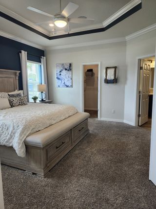 Model Home A cozy bedroom with plush carpet, a stylish tray ceiling, and a soft, inviting bed adorned with decorative pillows.