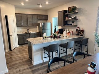 Model Home A modern kitchen with granite countertops, dark cabinetry, and open shelving, complemented by warm wood floors.