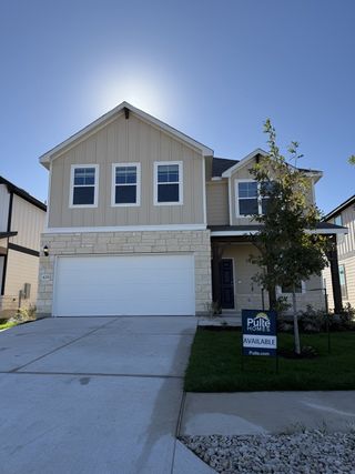 A modern tan home with a white garage and neat landscaping in Reserve at North Fork by Pulte Homes (Leander, TX).