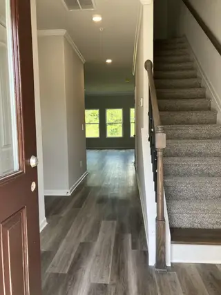A welcoming entryway with wood-look floors, neutral walls, and carpeted stairs leading to the second floor.