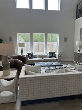 A bright living room with tall windows, woven sofa, modern decor, and ample natural light.