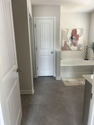A sleek bathroom with gray tile flooring, neutral walls, abstract art, and a white paneled door, creating a serene atmosphere.