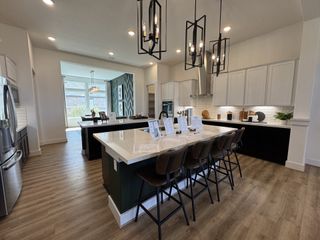A modern kitchen with a large island, pendant lighting, and sleek cabinetry, featuring an open dining area with natural light.