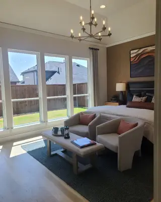 A cozy bedroom with large windows, modern chandelier, and stylish seating, creating a bright and inviting space.
