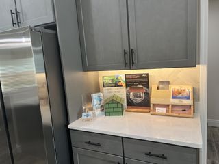 A modern kitchen corner with sleek gray cabinets, stainless steel fridge, and a marble countertop displaying brochures.