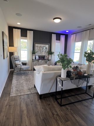 A cozy living room with elegant decor, featuring white sofas, wood flooring, and large windows with draped curtains.